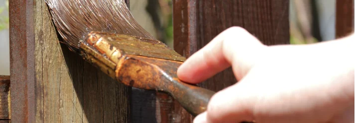 Person streicht Holzzaun mit Pinsel